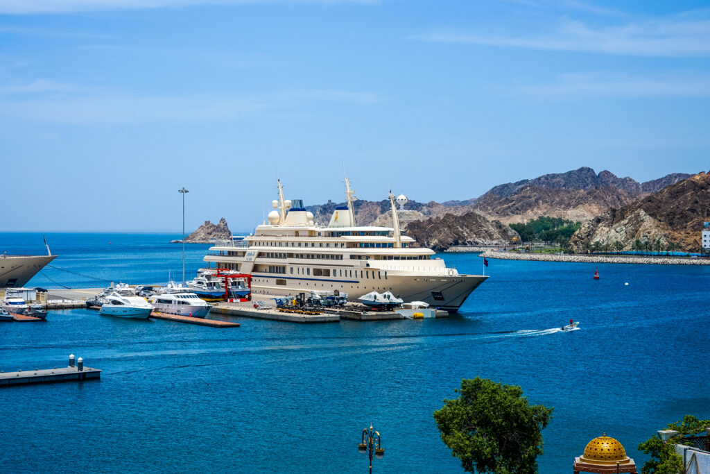 Al Said looms so large over neighboring boats at a dock in Muscat, Oman, that you could be forgiven for mistaking her for a cruise ship. The very tall white yacht with blue accents rests over a jewel-toned sea on a calm, sunny day.